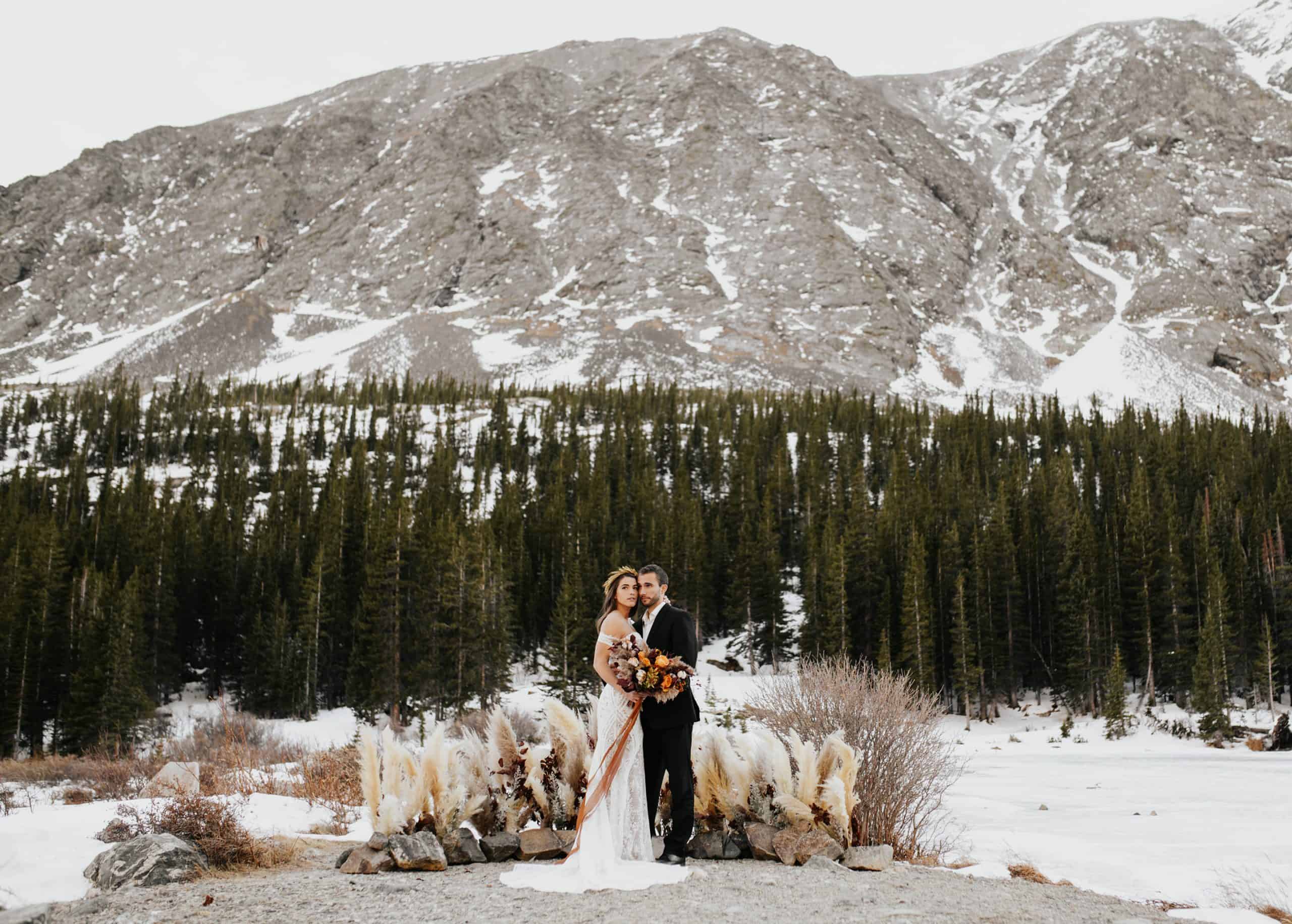 elopement newlyweds stand in front of floral ceremony site in the mountains