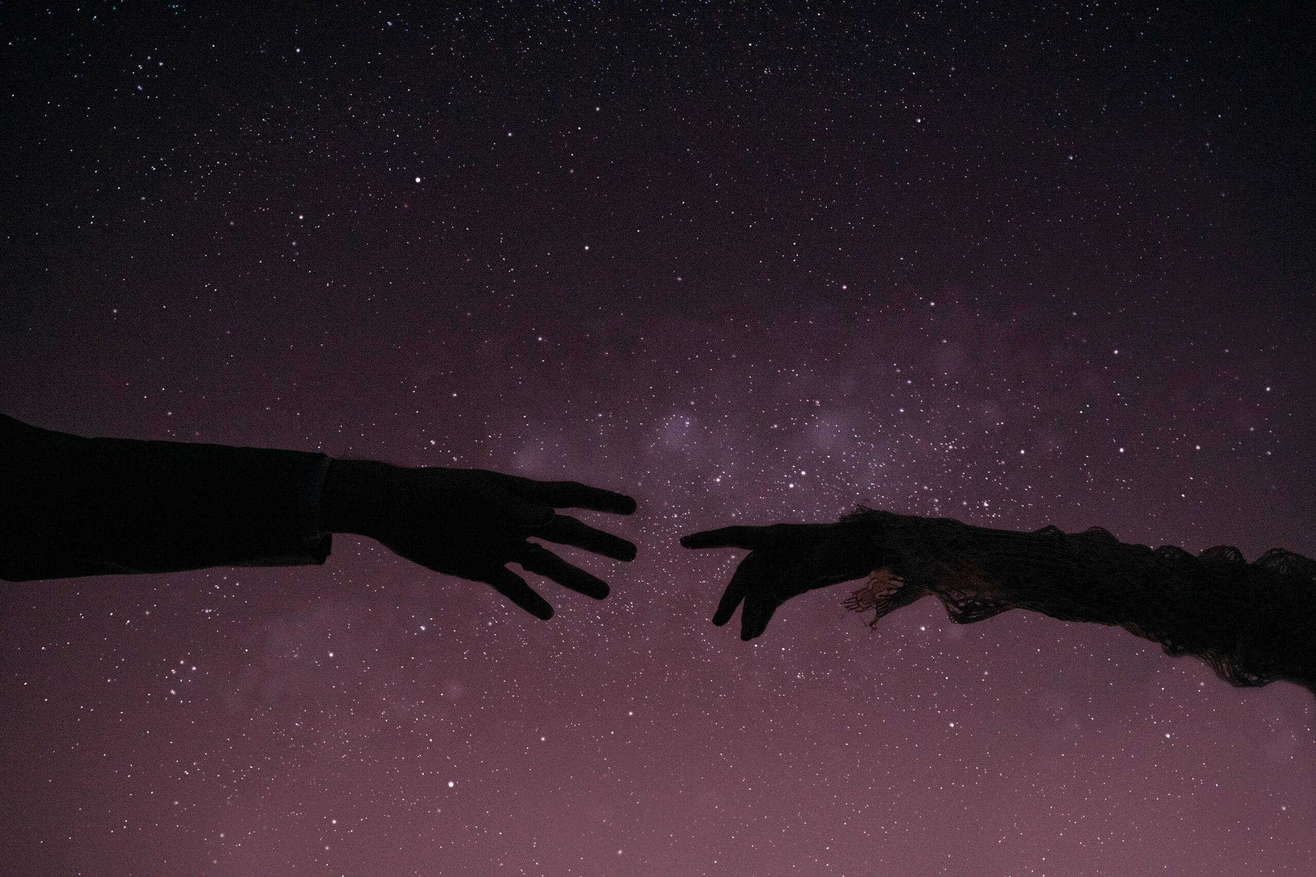 couples hands reach for each other in the dark underneath the starry night sky on blog dedicated to reasons to print your photos