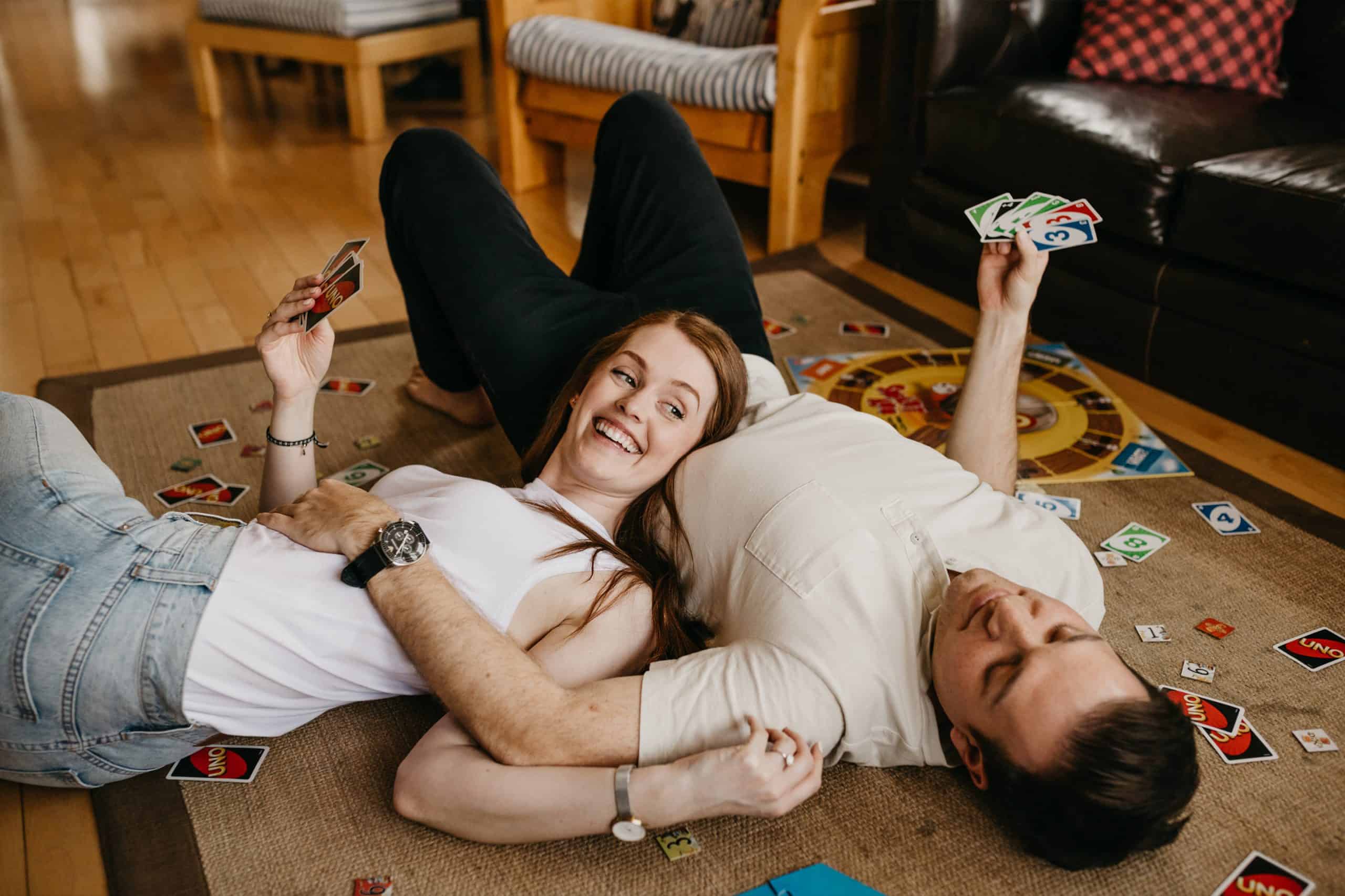 girl lays on the floor with her head on her boyfriends chest while they play Uno for an at home date night activity