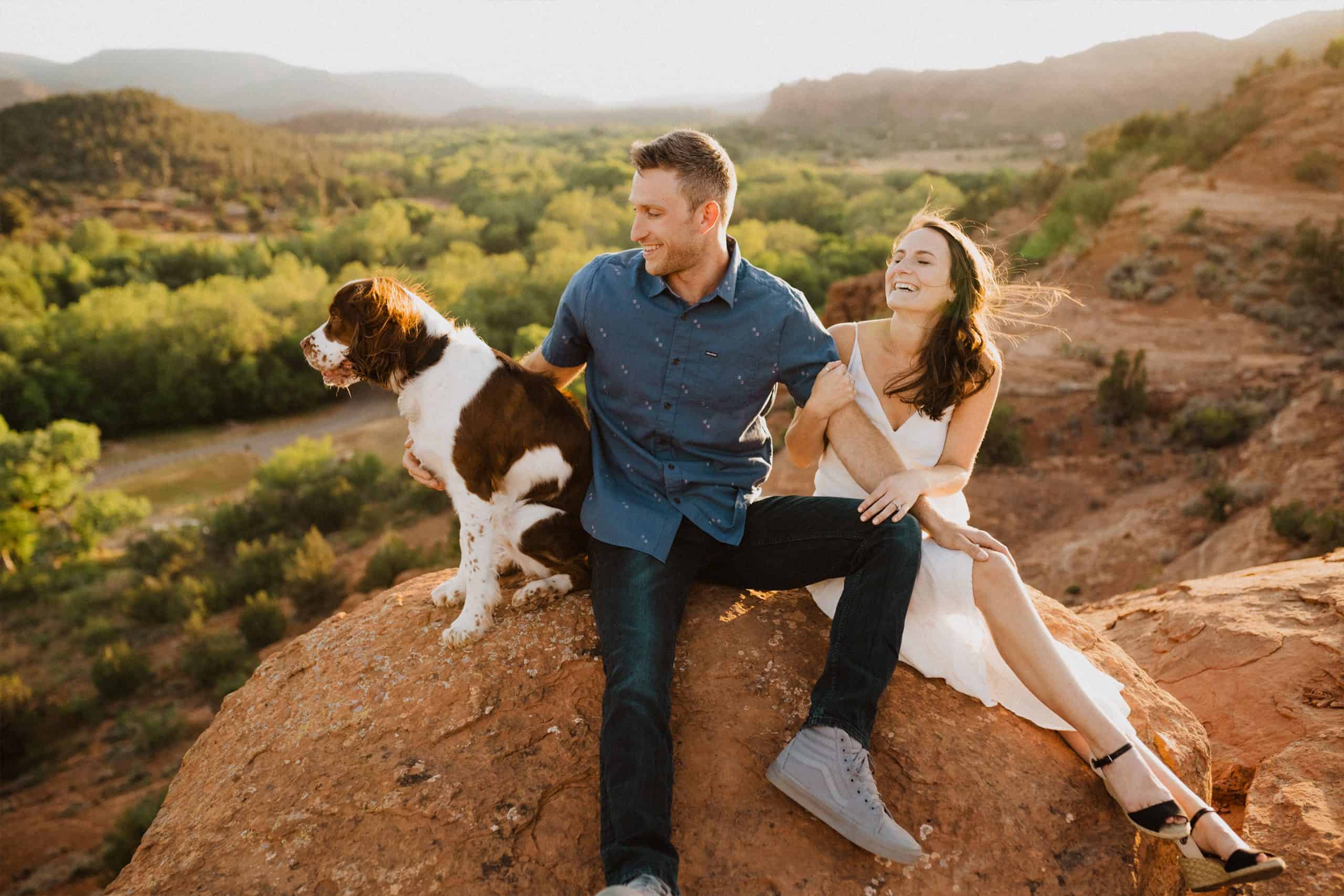 image of couple sit on a rock at sunset and play with their dog on blog for reasons to print your photos