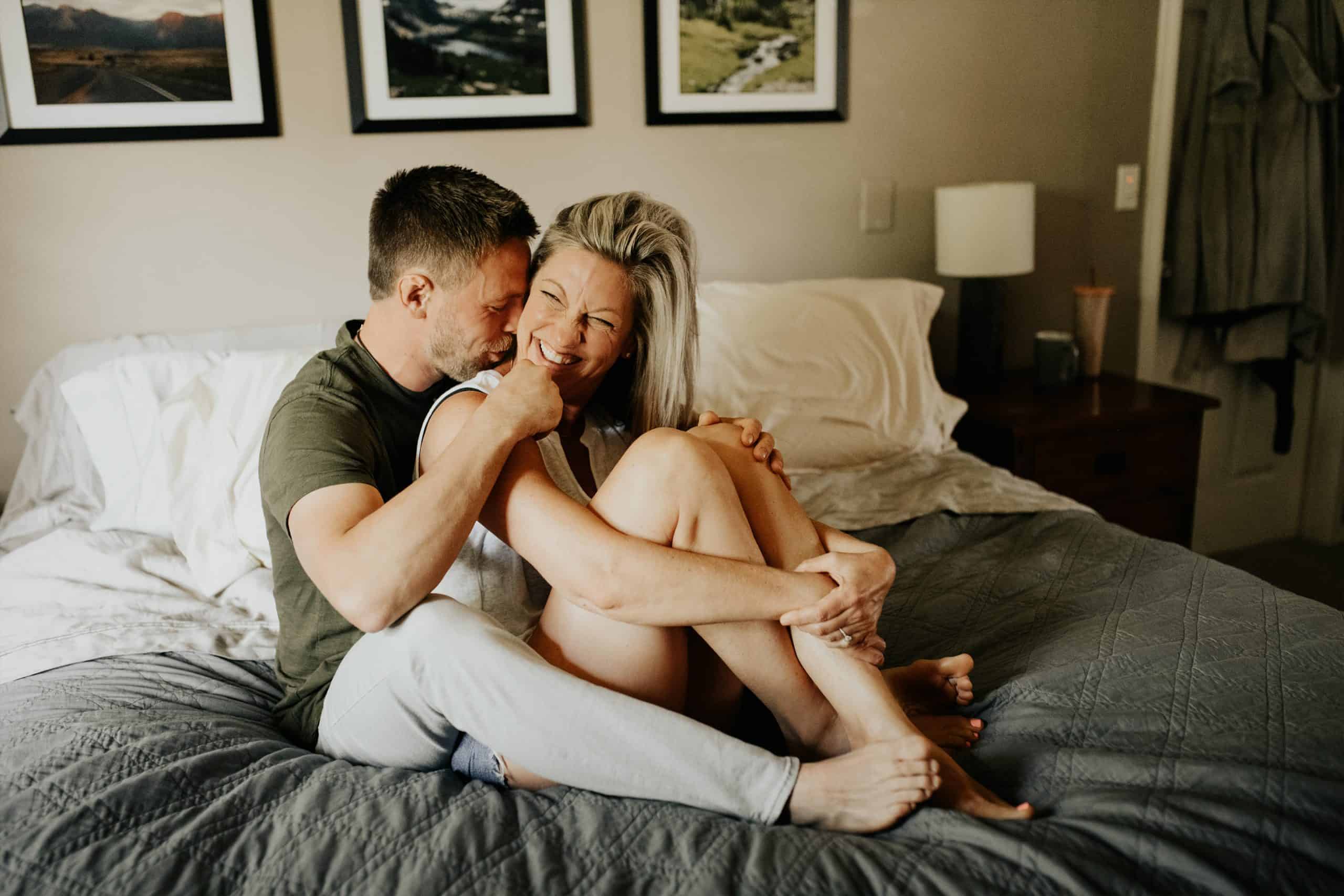 man and his wife snuggle in their bed and laugh