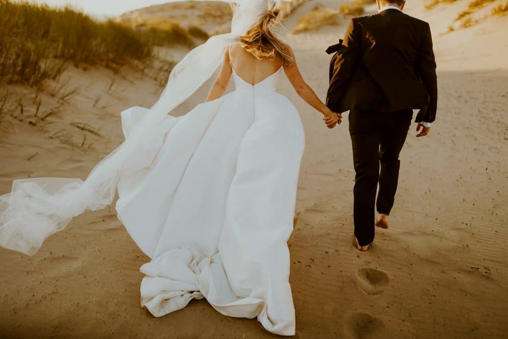 bride and groom hold hands as they walk on the beach after their sunset elopement