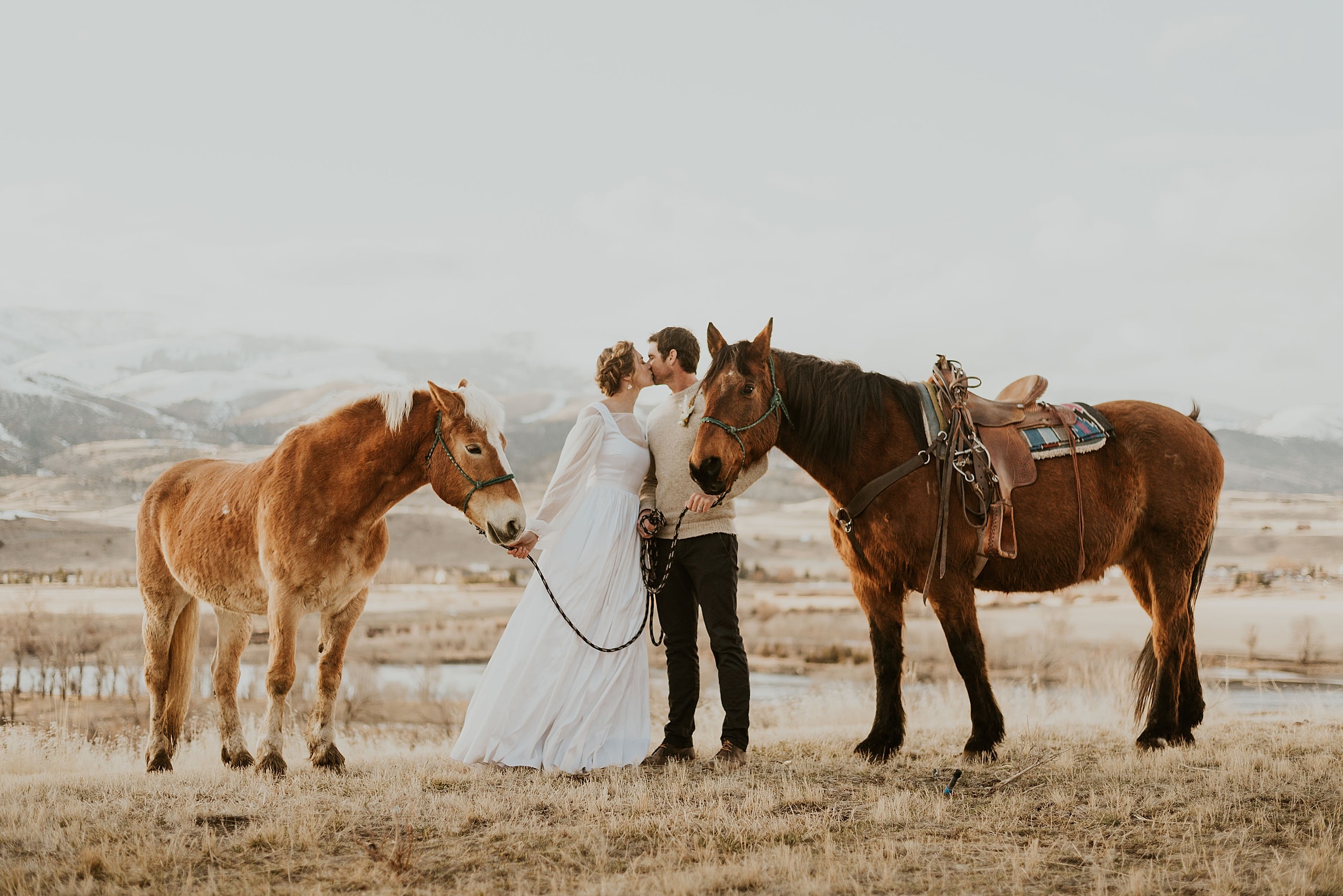 couple kissing while holding horses big sky montana landscape