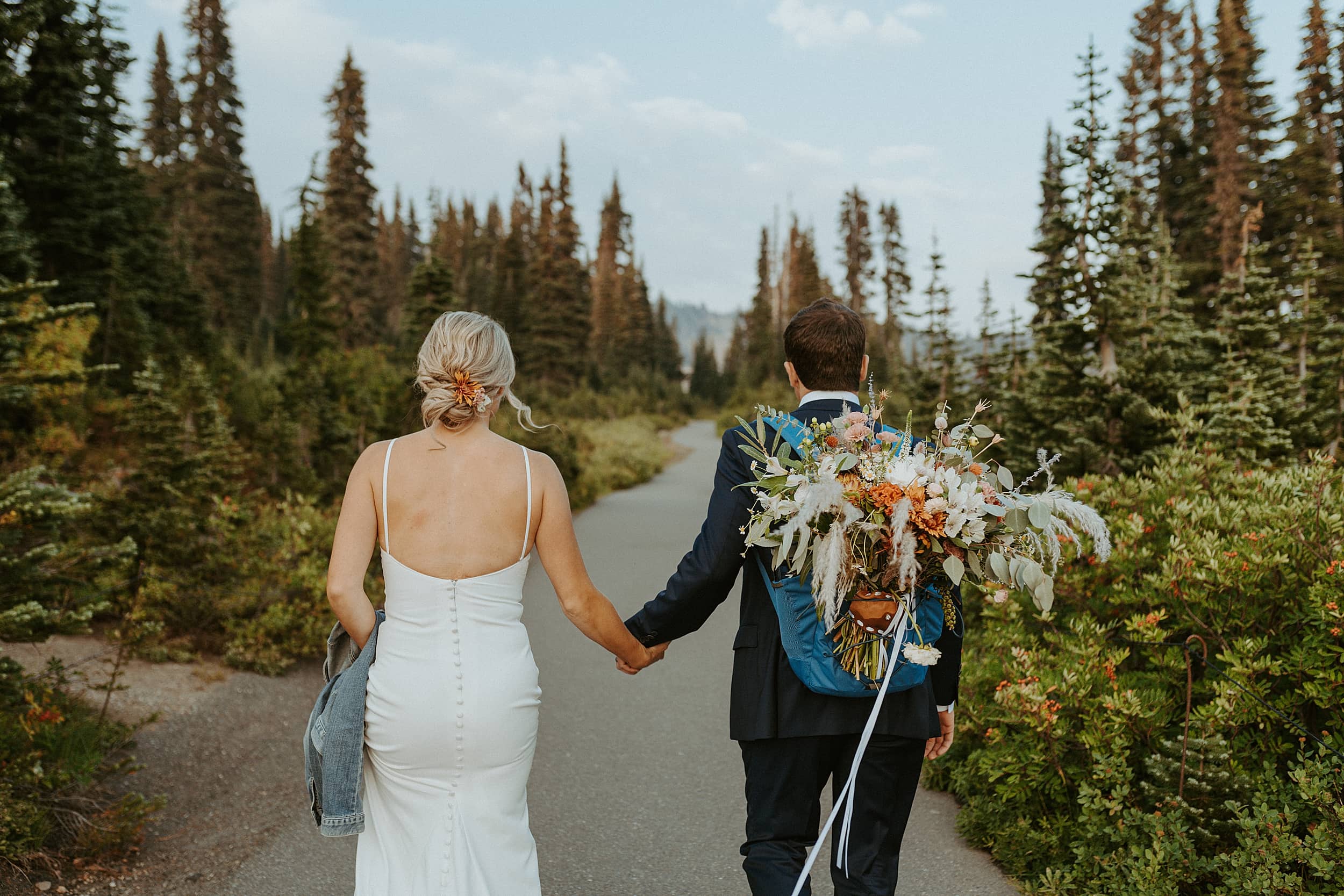 bride and groom walking together on forest trail with flower bouquet 